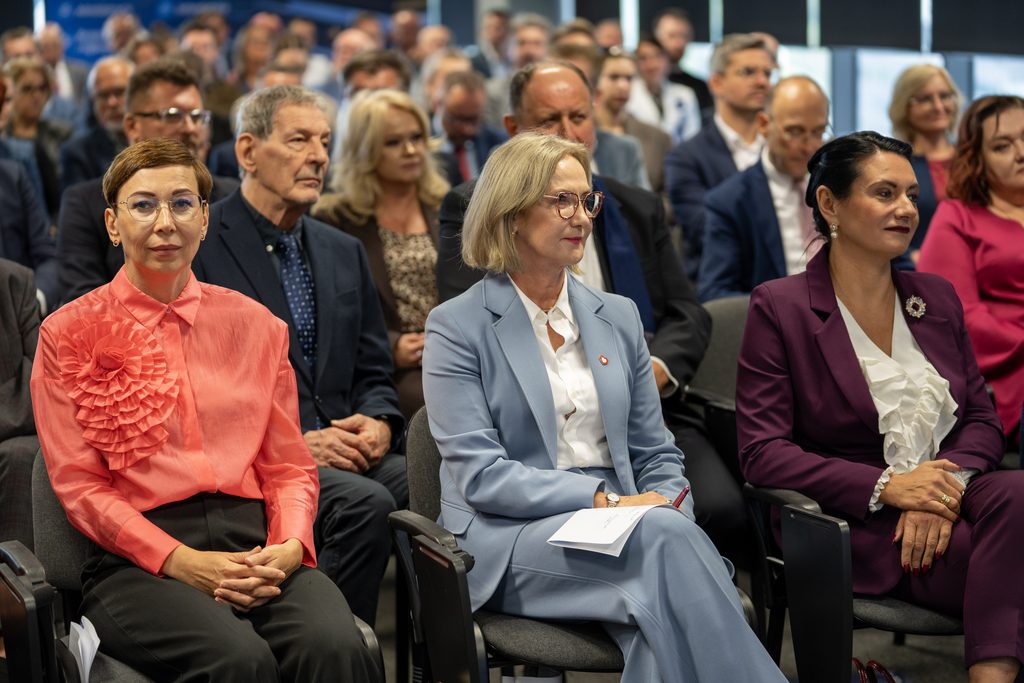 Uczestnicy wydarzenia Akademii Humanitas siedzą na widowni i słuchają wystąpienia. W pierwszym rzędzie widoczne są osoby w eleganckich strojach, a w tle znajduje się licznie zgromadzona publiczność.