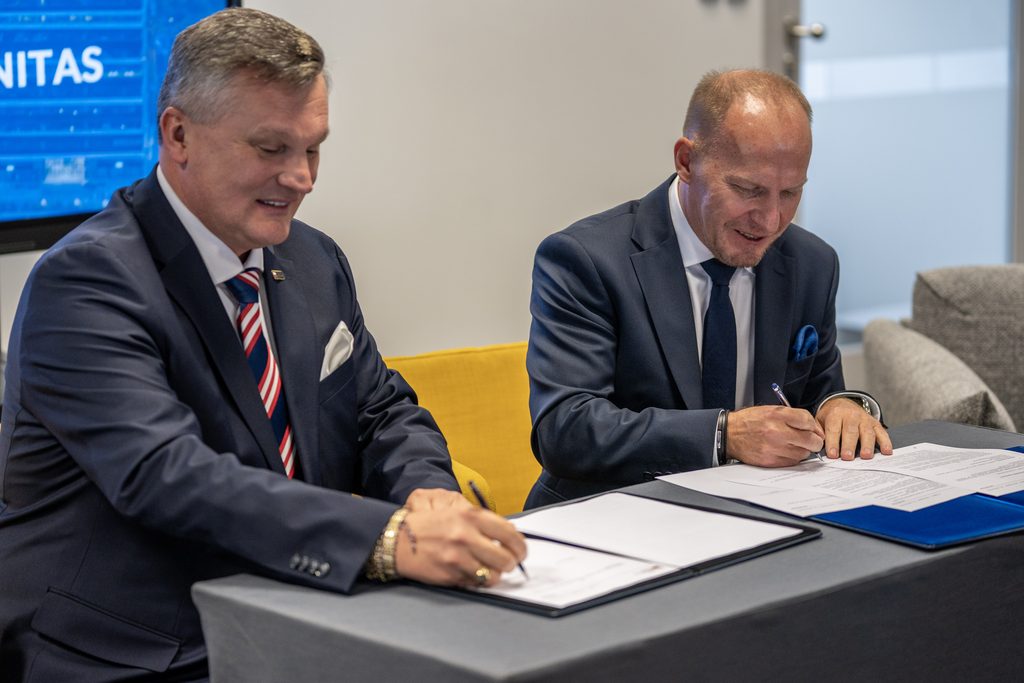 Przedstawiciele Akademii Humanitas i partnera wydarzenia podpisują dokumenty podczas uroczystego zawarcia porozumienia. Mężczyźni siedzą przy stole, składając podpisy na przygotowanych dokumentach.