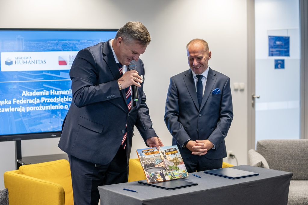 Przedstawiciele Akademii Humanitas i Śląskiej Federacji Przedsiębiorców Polskich podczas uroczystego podpisania porozumienia. Jeden z uczestników przemawia do mikrofonu przy stole z dokumentami.