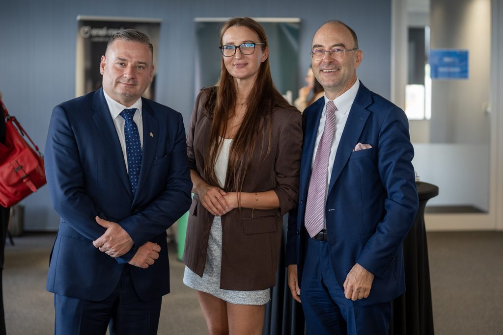 Trzy osoby pozują do zdjęcia podczas wydarzenia biznesowego Akademii Humanitas. Uczestnicy stoją w przestrzeni networkingowej, ubrani w eleganckie stroje.