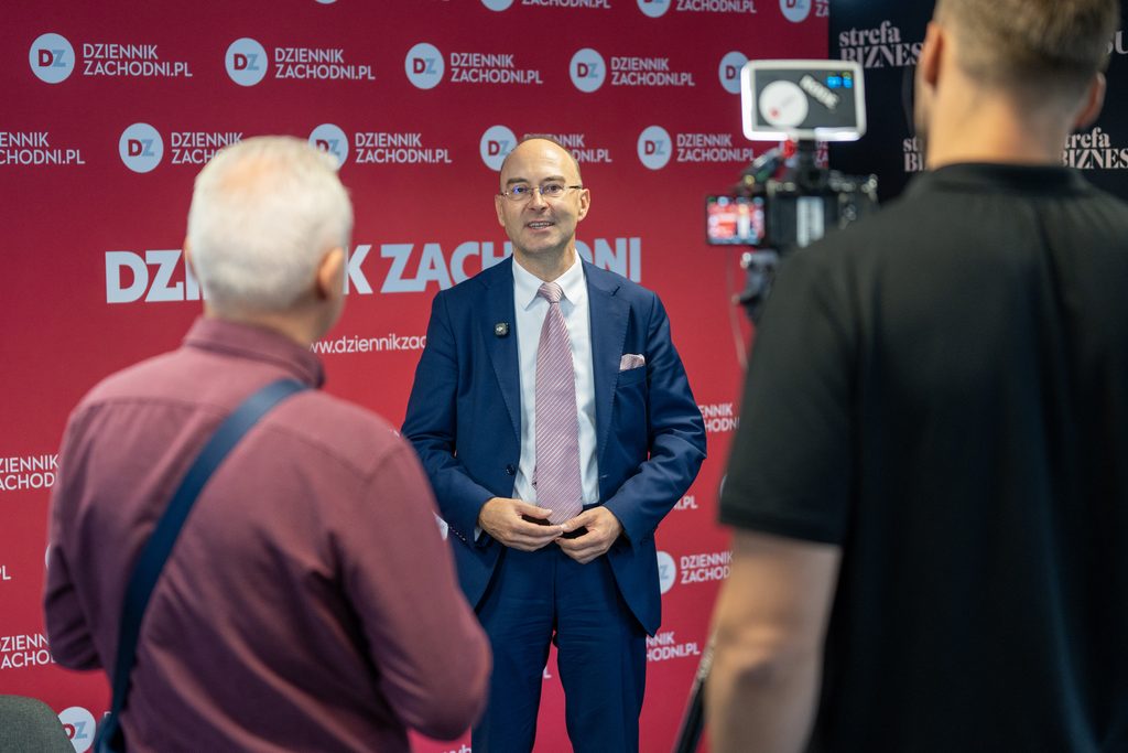 Uczestnik wydarzenia udziela wypowiedzi przed kamerą na tle ścianki Dziennika Zachodniego. W kadrze widoczni są także operatorzy nagrania i sprzęt filmowy.