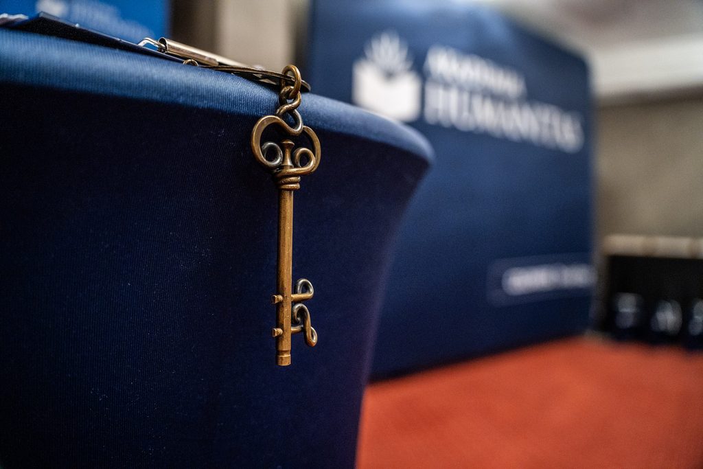 Zbliżenie na ozdobny klucz zawieszony przy granatowej tkaninie z logo Akademii Humanitas w tle.