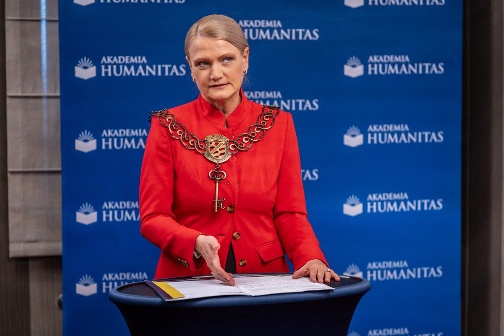 Przedstawicielka Akademii Humanitas w czerwonej marynarce i z insygniami uczelnianymi przemawia przy stoliku.