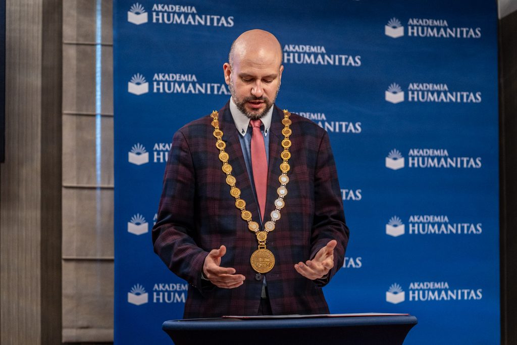 Mężczyzna z łańcuchem akademickim przemawia podczas uroczystości na tle ścianki Akademii Humanitas.