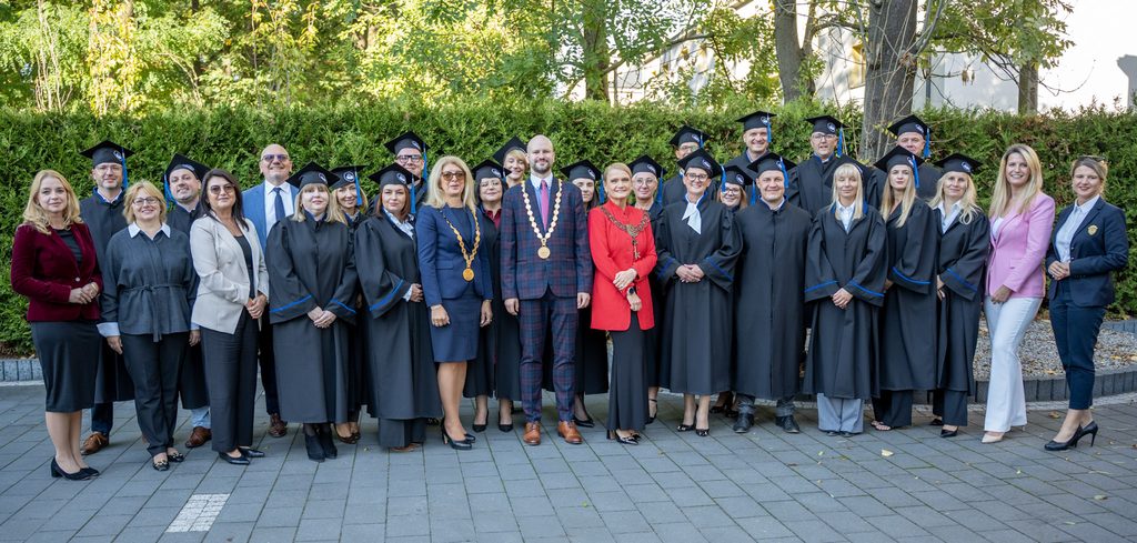 Grupowe zdjęcie uczestników Gali MBA Akademii Humanitas wykonane na zewnątrz. Część osób ubrana jest w togi i birety akademickie, a w centrum stoją przedstawiciele władz uczelni oraz zaproszeni goście.