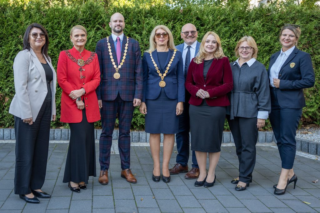 Grupowe zdjęcie przedstawicieli władz i kadry Akademii Humanitas wykonane na zewnątrz. Osoby pozują w eleganckich strojach, część z nich ma na sobie łańcuchy akademickie i insygnia uczelniane.
