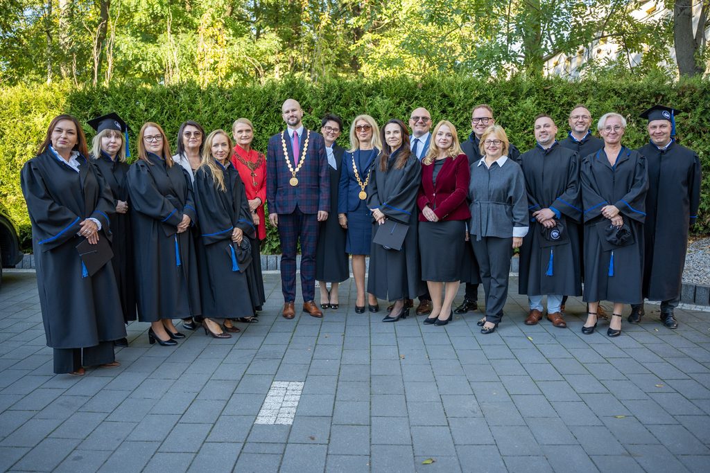 Uroczyste zdjęcie grupowe przedstawicieli Akademii Humanitas oraz absolwentów w togach, wykonane na zewnątrz.