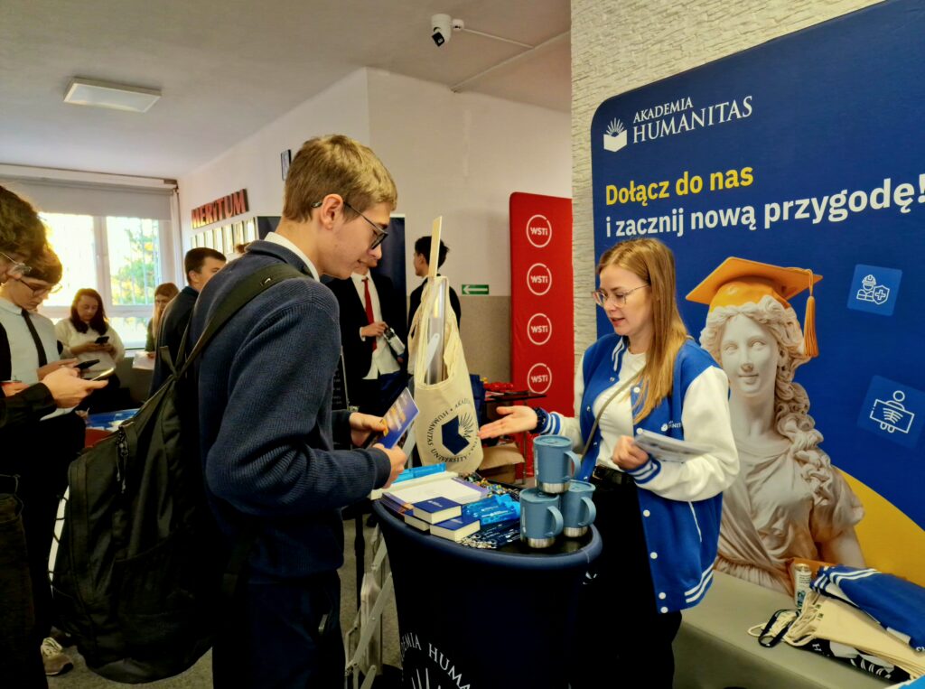 Przedstawicielka Akademii Humanitas rozmawia z uczniem o ofercie studiów przy stoisku promocyjnym uczelni podczas Dnia Kariery w MERITUM.