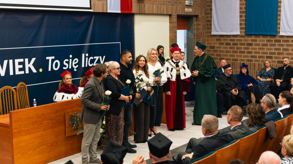 Laureaci Nagród Akademii Humanitas z dyplomami i białymi różami stoją obok Rektora dr. Mariusza Lekstona oraz Kanclerza Aleksandra Dudka podczas jubileuszowej inauguracji.