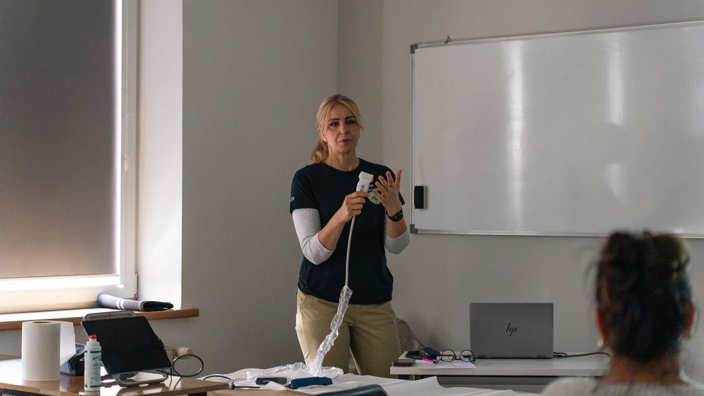 Prowadząca prezentuje uczestnikom warsztatów urządzenie diagnostyczne podczas zajęć praktycznych w sali szkoleniowej.