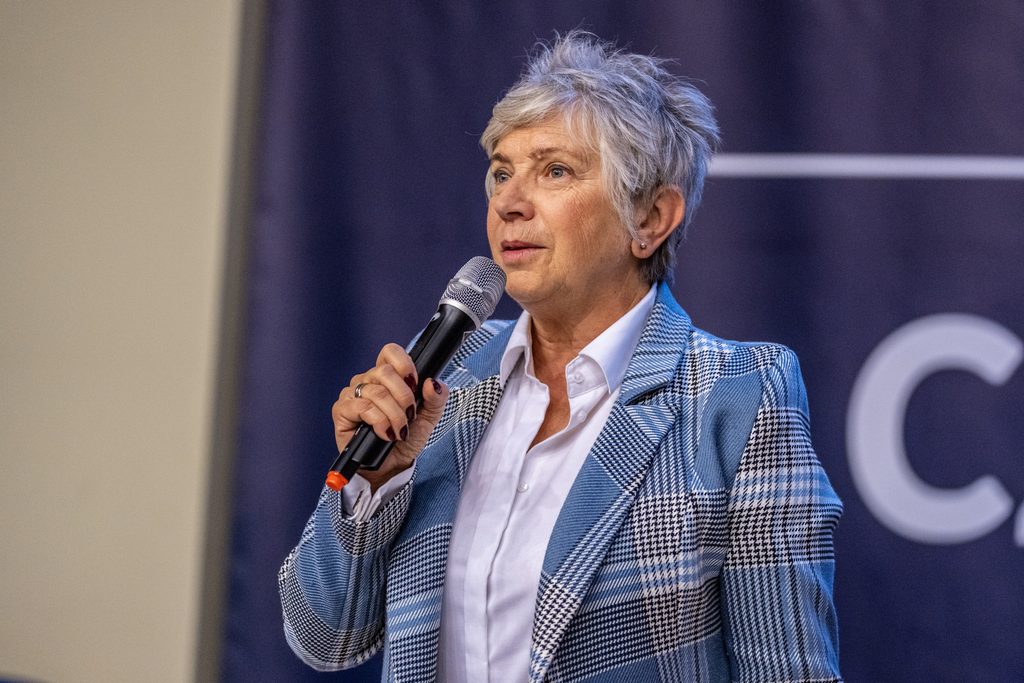 Prelegentka w niebieskiej marynarce przemawia z mikrofonem podczas wydarzenia Girls’ Week.