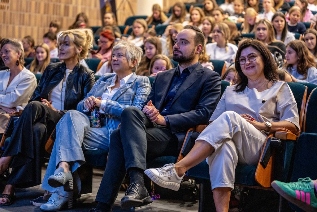 Uczestnicy i prelegenci siedzą w pierwszym rzędzie auli podczas Girls’ Week, w tle widoczna publiczność.