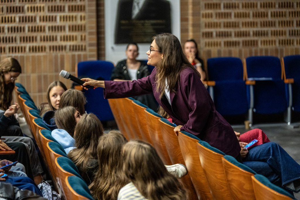 Prowadząca przekazuje mikrofon uczestniczce wydarzenia Girls’ Week w auli Akademii Humanitas.