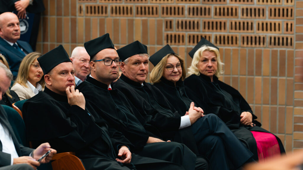 Członkowie społeczności akademickiej w czarnych togach i biretach uczestniczą w jubileuszowej inauguracji roku akademickiego Akademii Humanitas, siedząc wśród zaproszonych gości.