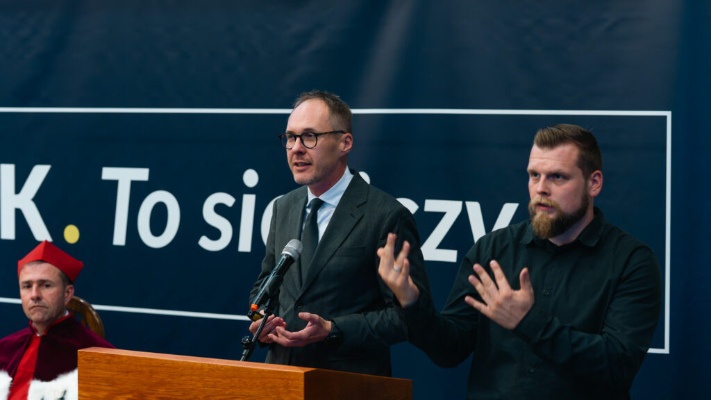Dr hab. Marcin Zajenkowski, prof. Uniwersytetu Warszawskiego, wygłasza wykład inauguracyjny podczas uroczystości w Akademii Humanitas. Obok tłumacz języka migowego przekłada wystąpienie.