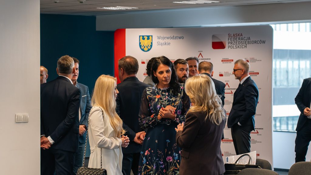 Grupa uczestników wydarzenia prowadzi rozmowy networkingowe na tle ścianki Województwa Śląskiego i Śląskiej Federacji Przedsiębiorców Polskich.