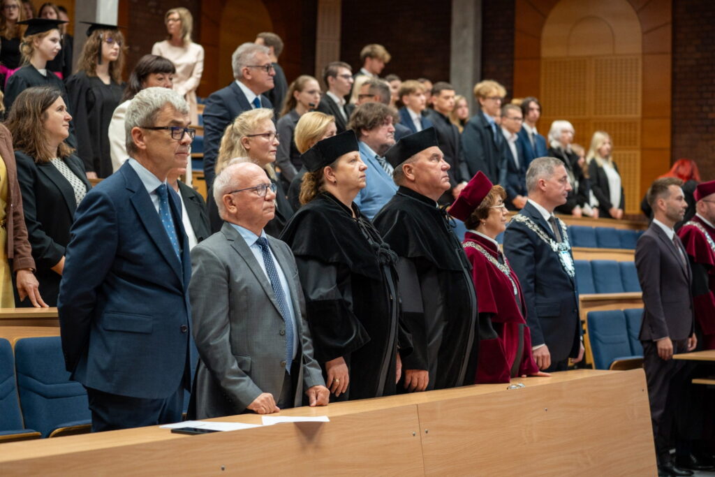 Przedstawiciele władz uczelni, zaproszeni goście i studenci stoją w auli podczas uroczystej inauguracji roku akademickiego w Rybniku.
