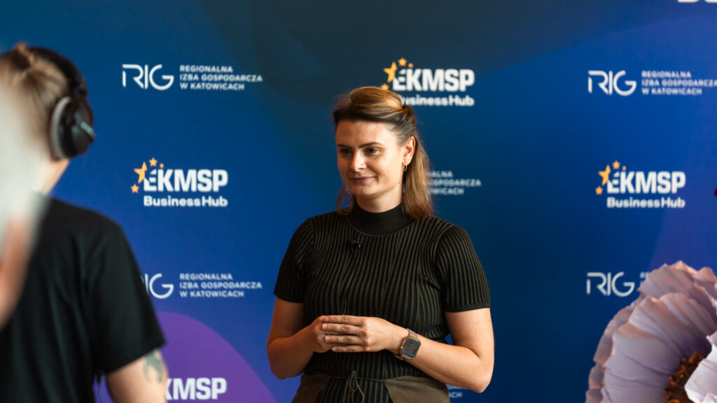 Ekspertka Akademii Humanitas udziela wywiadu na tle ścianki z logotypami Europejskiego Kongresu MŚP i Regionalnej Izby Gospodarczej w Katowicach.