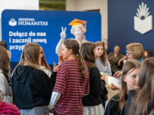 Uczestniczki wydarzenia Girls’ Week rozmawiają podczas spotkania w Akademii Humanitas; w tle widoczna jest ścianka promocyjna uczelni z hasłem „Dołącz do nas i zacznij nową przygodę!”
