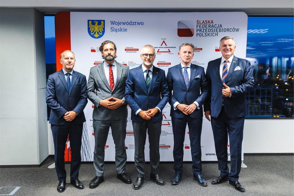 Pięciu uczestników wydarzenia pozuje do pamiątkowego zdjęcia na tle ścianki partnerskiej.